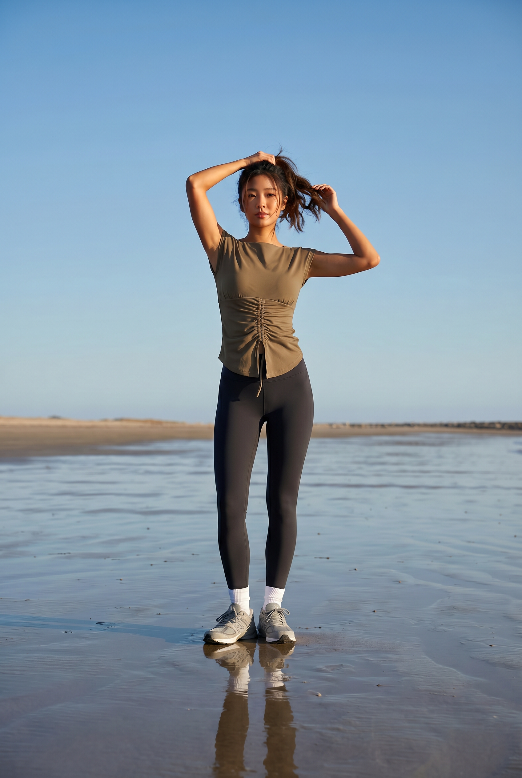 Woman standing on a beach wearing a green top and black leggings.